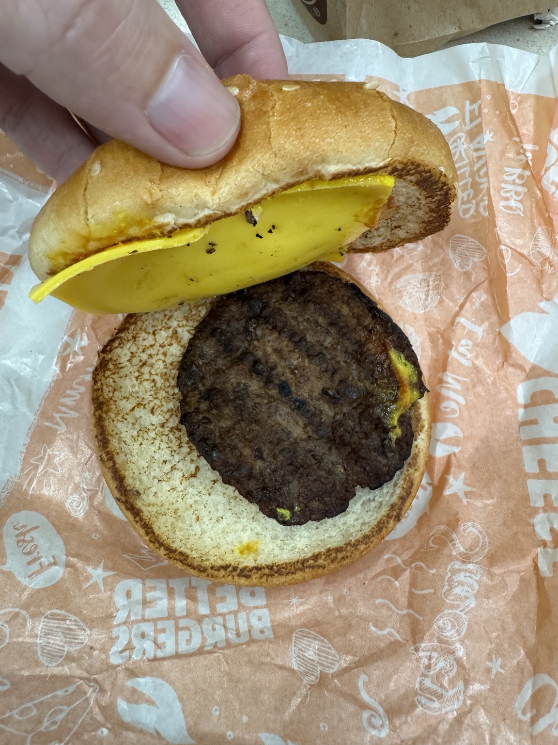 A Hungry Jack's cheeseburger with a small patty and largely unmelted cheese, opened to show the contents.